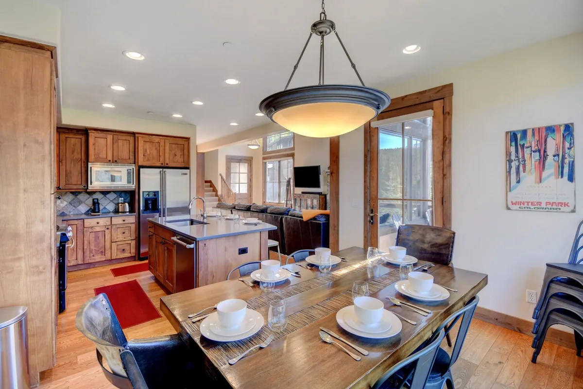 A bright, welcoming interior dining space with a large table set for a meal, a modern kitchen island, and expansive windows letting in abundant natural light. The scene exudes warmth, comfort, and an inviting atmosphere for year-round gatherings.