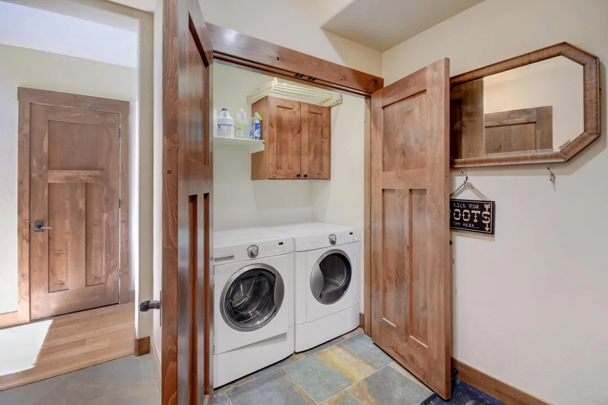 This scene shows a neatly organized laundry area featuring a washer and dryer, wooden cabinetry, mirror, and slate flooring. The area looks practical yet cozy, supporting the idea of keeping everyone fresh for new adventures.