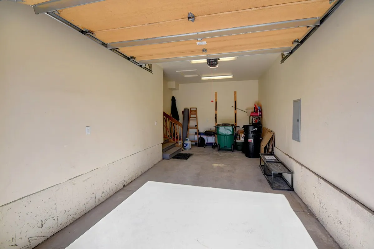 A practical interior space featuring the garage door, a staircase, storage items, and garbage bins. The area is open and uncluttered, suggesting convenient parking and easy transition into the home, especially for those needing direct access.