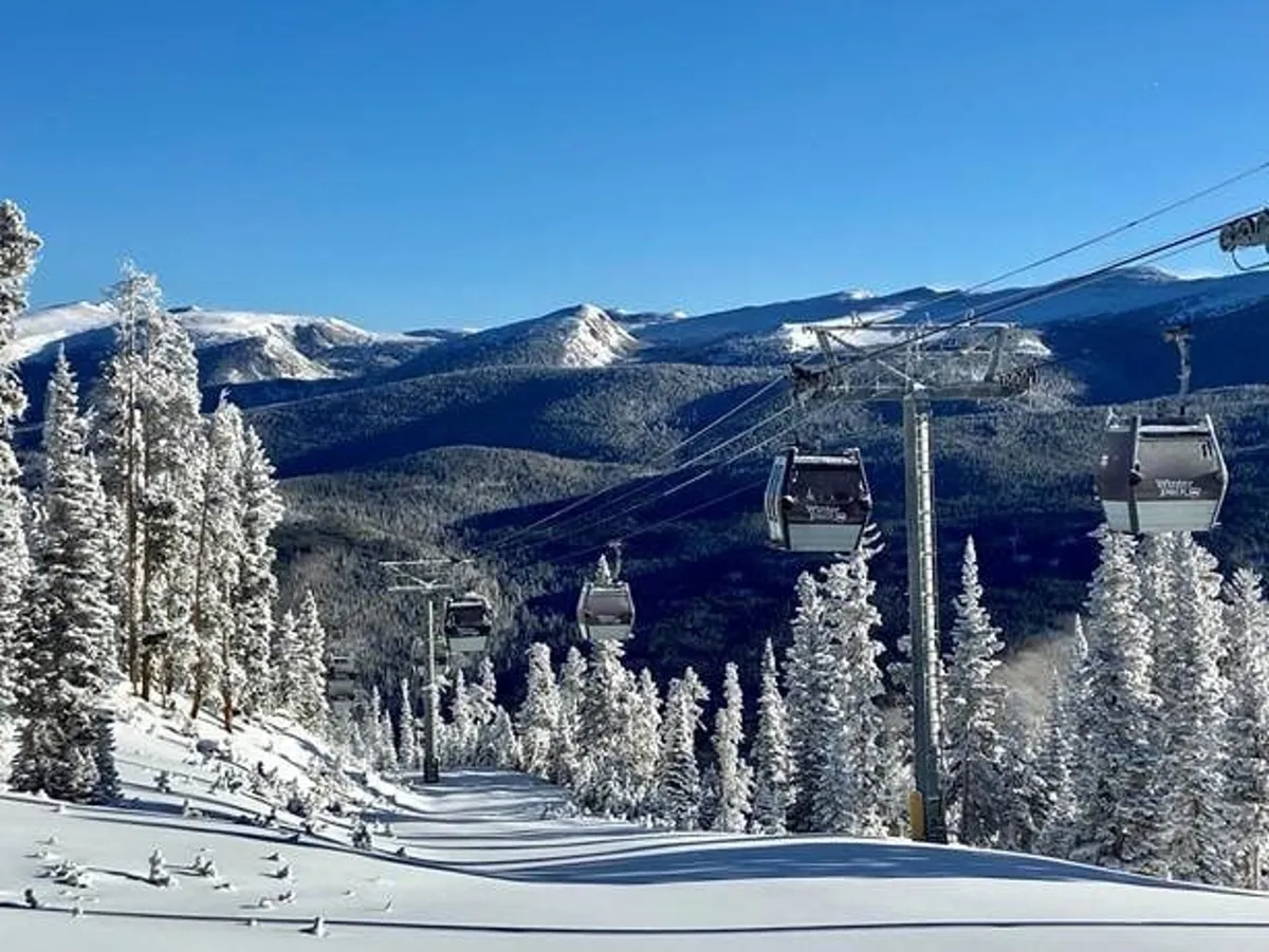 This image features ski lift gondolas ascending over a snow-covered landscape, with snow-laden trees and a picturesque mountain range in the background. The scene is tranquil yet full of winter adventure potential, embodying the mountain resort experience.