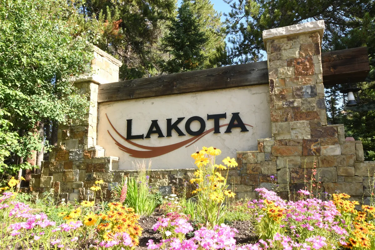 This image presents the LAKOTA sign at the villa's entrance, complemented by vibrant flower beds and a sturdy stone structure. The scene is bathed in natural light, with well-maintained landscaping suggesting a welcoming and accessible environment.