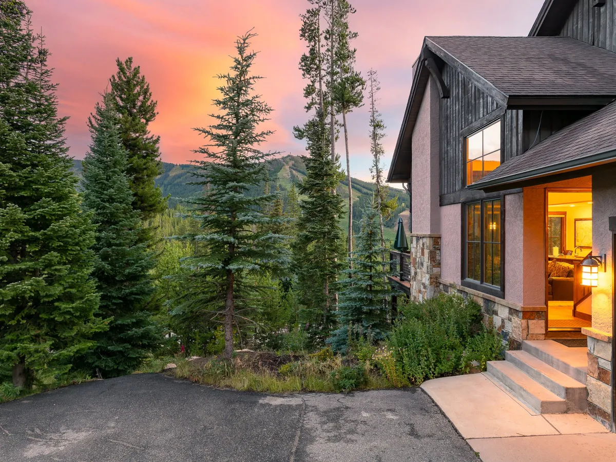 The photo showcases a beautiful sunset over a stone entrance, surrounded by trees and mountain views, exuding a welcoming and serene atmosphere.
