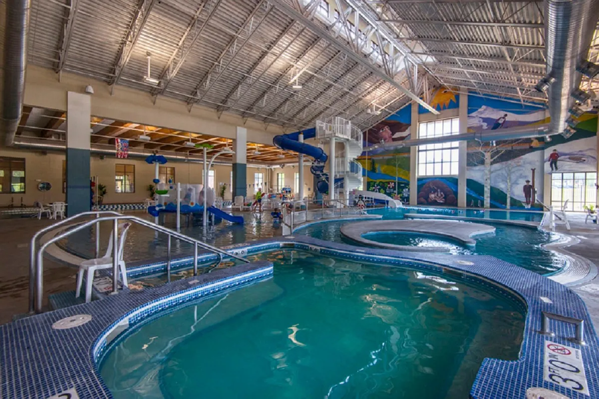 An energetic indoor swimming pool scene featuring colorful water slides, playful murals, and children laughing and splashing in the water. The space is lively and designed for family fun, making it ideal for group activities and entertainment for kids of all ages.