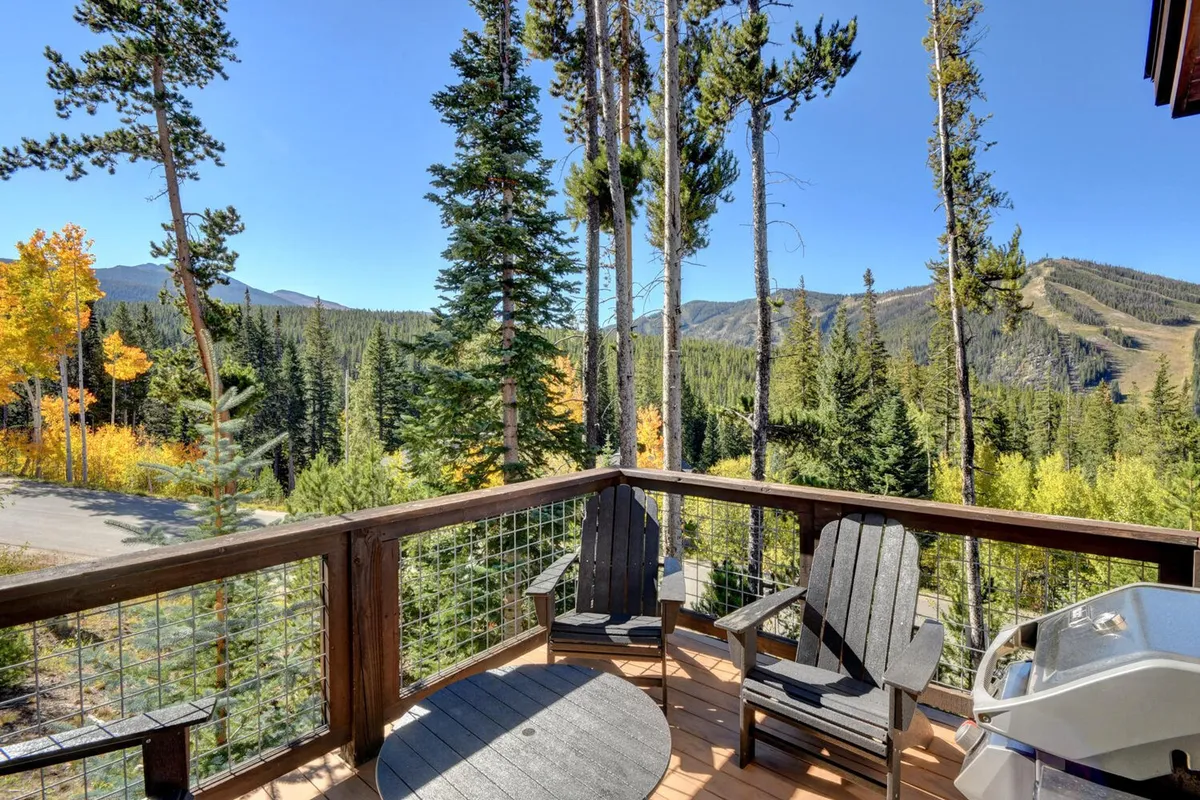 A peaceful deck area set among the trees, outfitted with deck chairs and a grill, overlooking a breathtaking mountain landscape. The setting invites relaxation, morning coffee, or stargazing, highlighting both comfort and the close connection to nature.