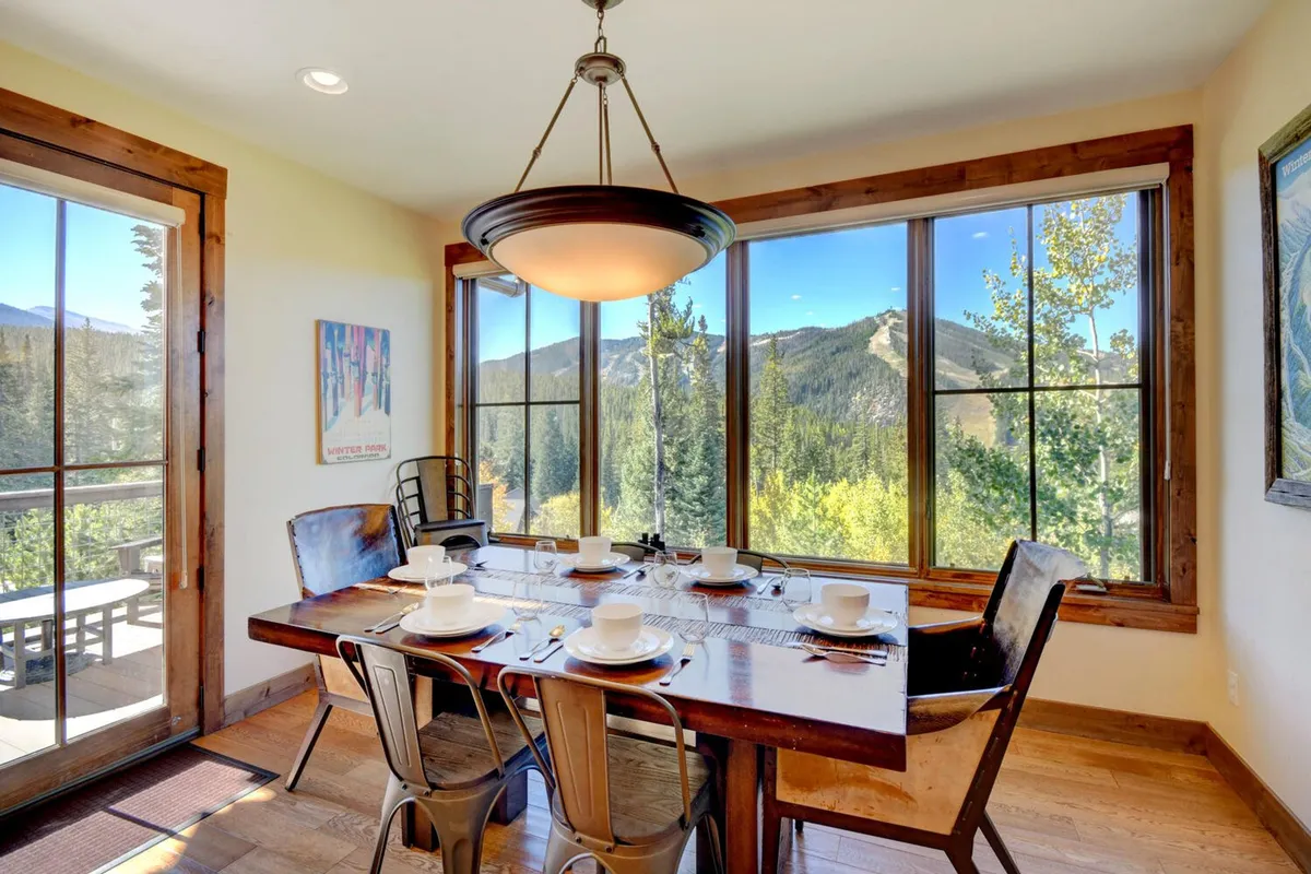 The dining area features a spacious table set beside large windows that frame breathtaking mountain views. Decorative wall art and warm lighting create a welcoming setting for memorable family meals, echoing the 'luxury treehouse' feel highlighted in the text.