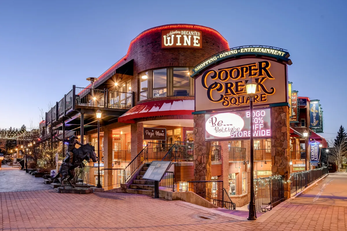 An inviting outdoor shopping plaza with the Cooper Creek Square sign, festive decorative lighting, cozy outdoor seating, and a welcoming atmosphere perfect for families exploring, dining, and enjoying local events.