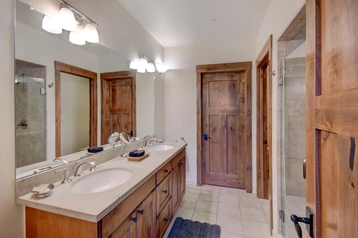 A spa-like bathroom with double vanity sinks, a large mirror, wooden cabinetry, and a glass shower enclosure. The inviting atmosphere suggests relaxation and comfort after outdoor activities.