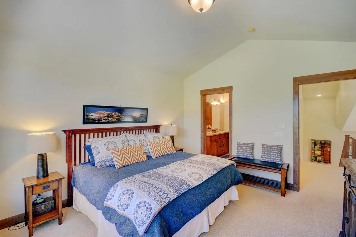 A cozy bedroom with a queen bed dressed in patterned bedding, nightstands with lamps, and framed artwork. The ambiance is warm and tranquil, ideal for a restful night or quiet reading.