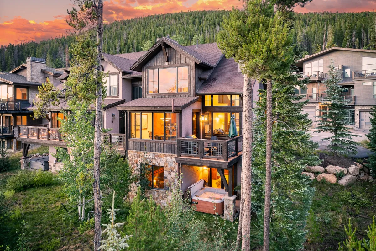 This exterior image showcases a modern mountain villa with large windows and balconies nestled among trees, featuring a prominent hot tub with panoramic mountain views in the background. The setting exudes privacy and luxurious relaxation, with direct visual access to the surrounding wilderness.