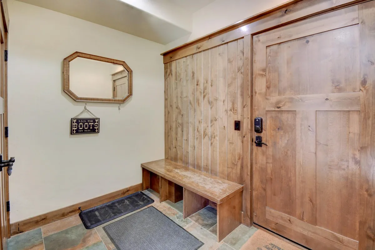 This image captures a cozy, welcoming mudroom with a wooden bench, decorative mirror, entry door, and a welcome sign. It's a practical space for removing and storing outdoor gear after a day on the slopes or trails, and sets a warm, inviting tone upon entry.