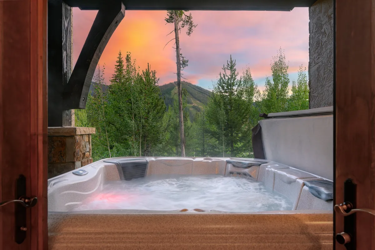 This view features a bubbling hot tub on a deck facing stunning mountain views at sunset. It's a tranquil, private spot for soaking muscles after a day of adventure, with the natural beauty of the mountains all around.