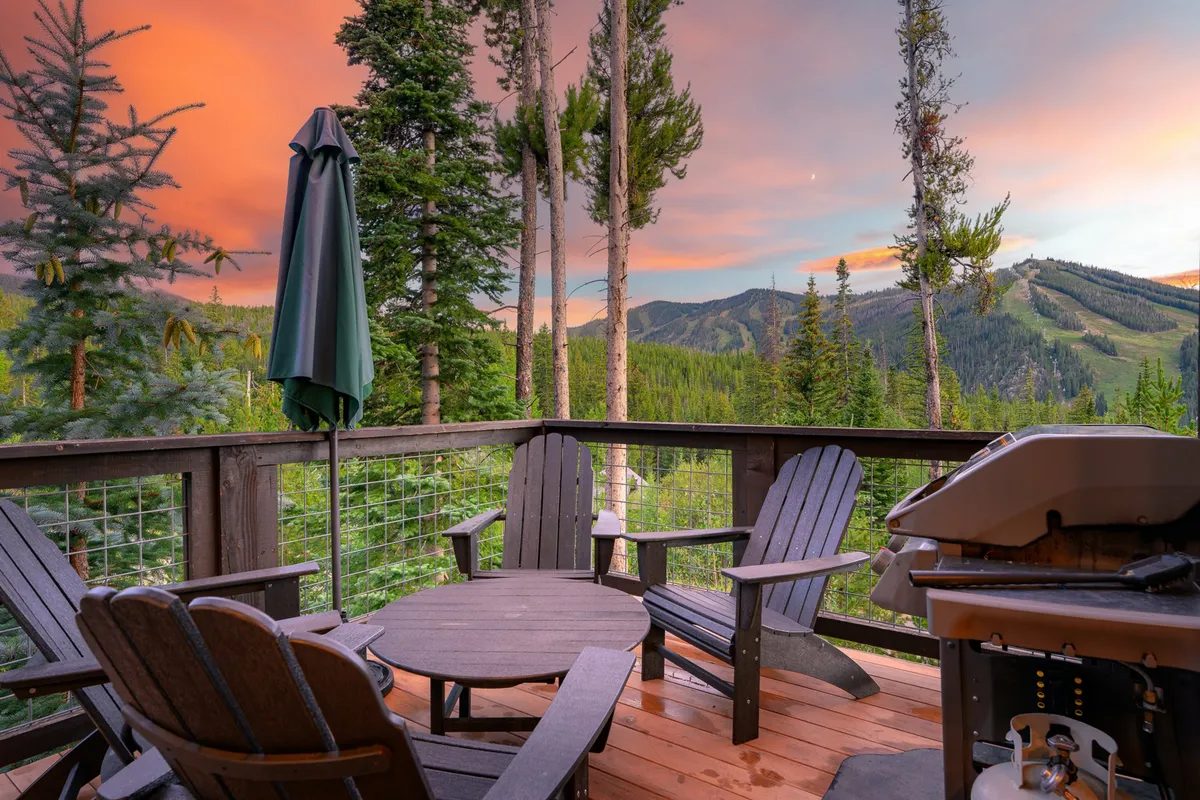 A stylish outdoor deck featuring comfortable seating, a propane grill, and a sweeping mountain view. The area is bathed in the soft glow of a sunset sky, creating a tranquil setting for alfresco dining or relaxing with family and friends.